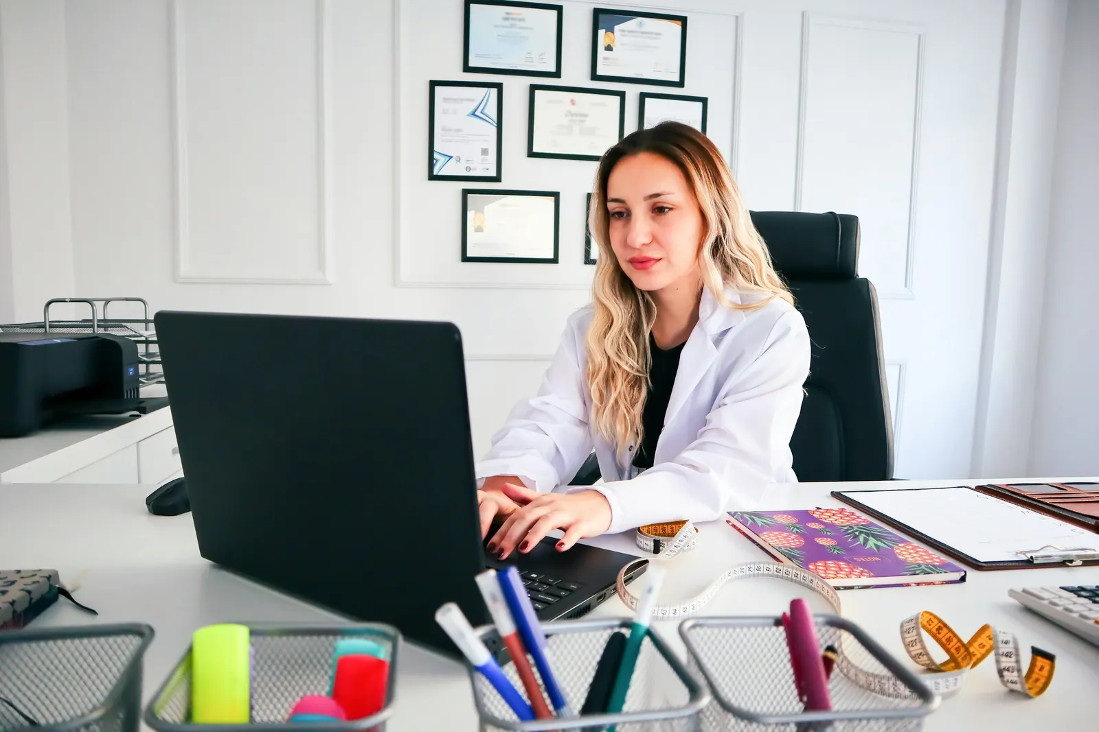 Profesional de la salud con guardapolvo trabajando en una laptop sobre un escritorio ordenado y luminoso